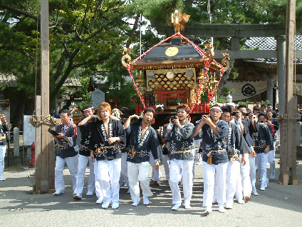 男衆が鳥居前で神輿を担ぐ様子